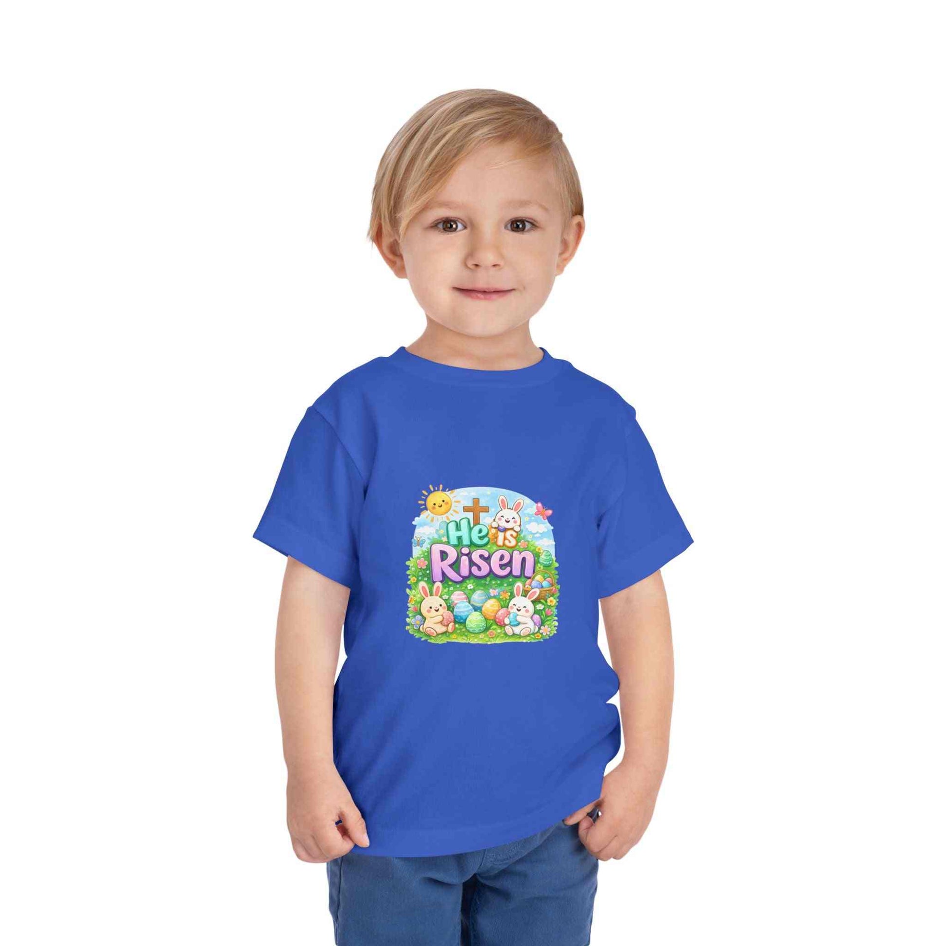 He Is Risen toddler tee with Easter bunny, cross, and eggs illustration on soft pastel fabric