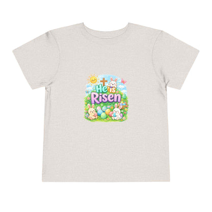 He Is Risen toddler tee with Easter bunny, cross, and pastel eggs design for kids