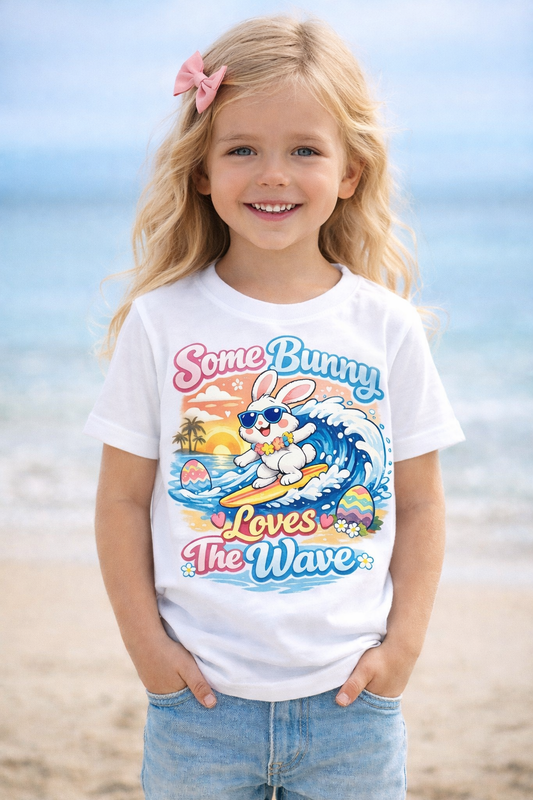 Surfing bunny Easter T-shirt with pastel eggs and sunset wave background, titled Some Bunny Loves The Wave.